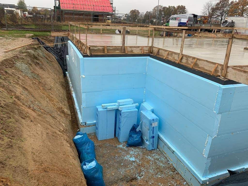 Blaue Perimeterdämmplatten an der Außenwand eines Kellers in der offenen Baugrube